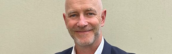 Gregor Zowierucha, CEO der PLATH GmbH & Co. KG, lächelt in die Kamera. Er trägt einen dunklen Anzug mit weißem Hemd. Der Hintergrund ist ein Büro.